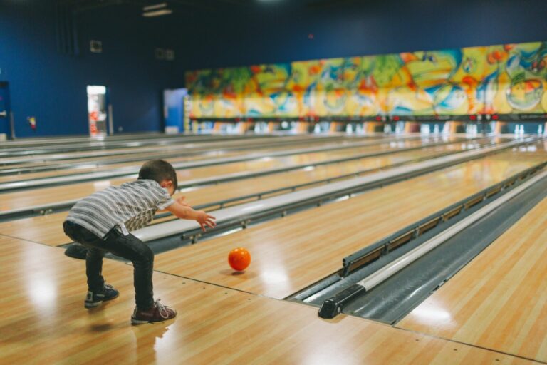 A little boy throwing a bowling ball down a lane at the bowling alley.